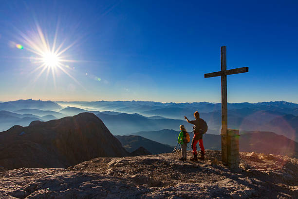 father and daughter enjoy the sunrise at mountain peak hochkönig - summit cross imagens e fotografias de stock