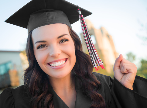 Happy Graduating Mixed Race Woman In Black Cap and Gown Celebrating on Campus.