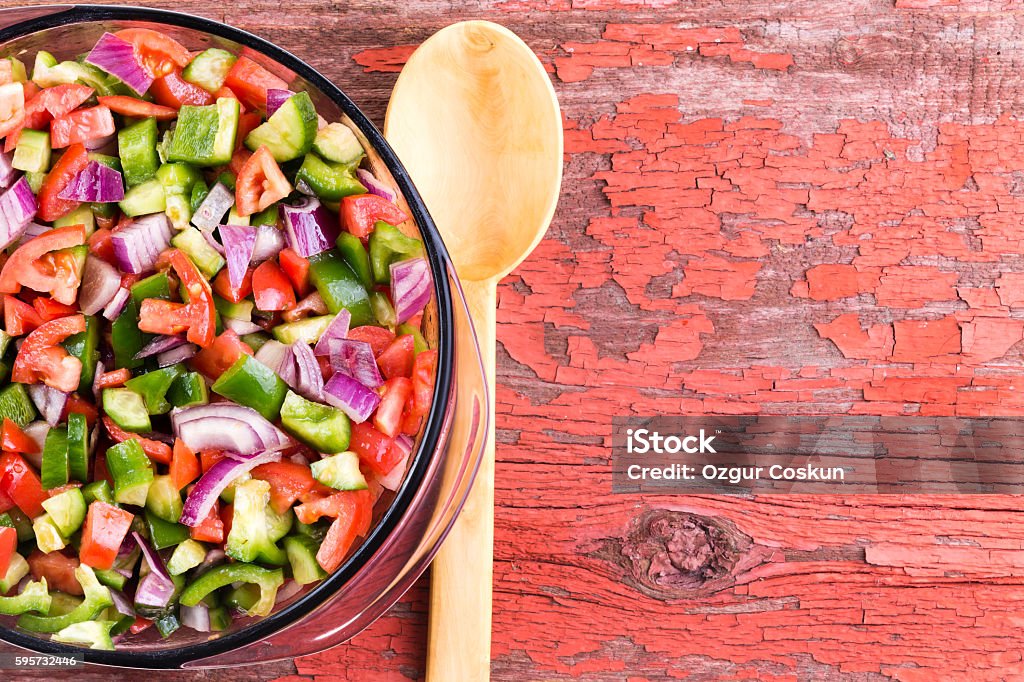 Bowl of healthy traditional Turkish shepherd salad Bowl of healthy traditional Turkish shepherd salad with colorful finely diced assortment of fresh vegetables with a wooden serving spoon on an old grungy red picnic table with copy space Chopping Food Stock Photo