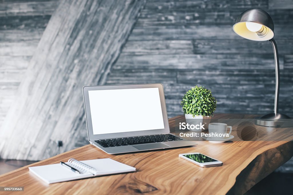 Creative wooden desktop Wooden designer desktop with blank white laptop, stationery items, coffee cup, cell phone, plant and table lamp. Mock up Table Stock Photo