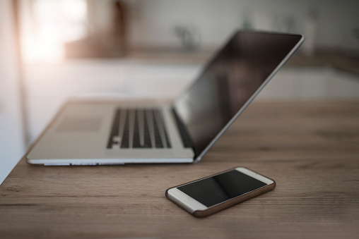 Open Laptop and Smartphone on Wooden Table in the Kitchen.