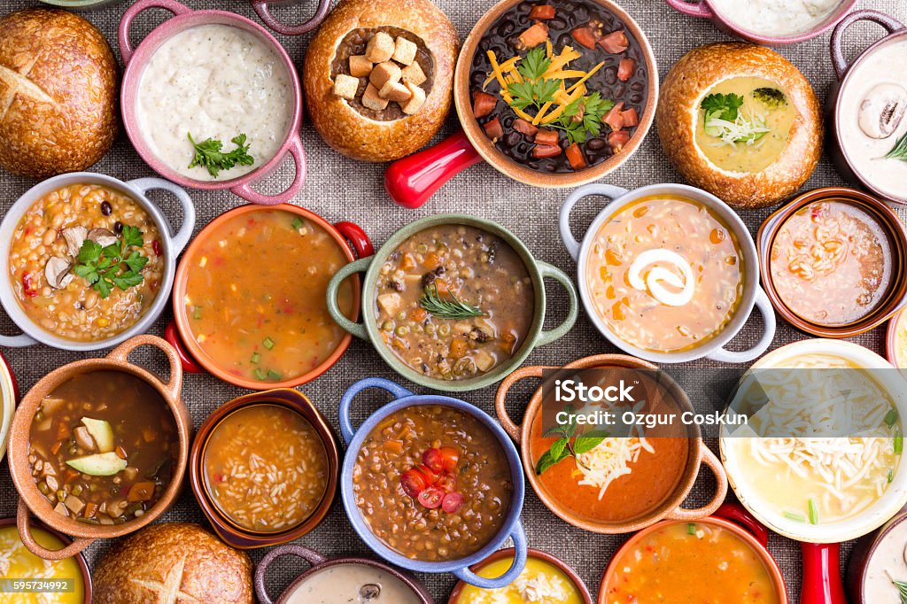 Variety of Garnished Soups in Colorful Bowls High Angle View of Various Comforting and Savory Gourmet Soups Served in Bread Bowls and Handled Dishes and Topped with Variety of Garnishes on Table Surface with Gray Tablecloth Soup Stock Photo