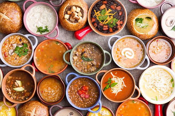 Variety of Garnished Soups in Colorful Bowls High Angle View of Various Comforting and Savory Gourmet Soups Served in Bread Bowls and Handled Dishes and Topped with Variety of Garnishes on Table Surface with Gray Tablecloth savory food photos stock pictures, royalty-free photos & images