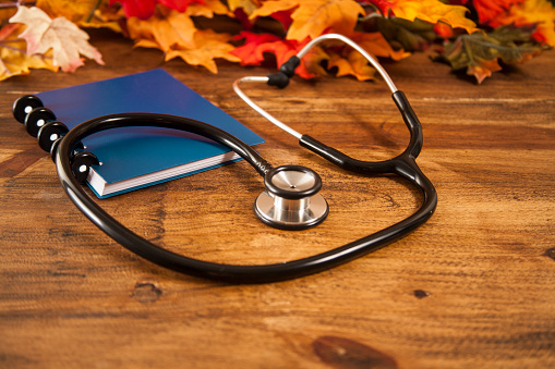 Close up view of a doctor's stethoscope, pen, and blue notepad or notebook with autumn leaves.  No people.  Medical, healthcare, studying, check-up, back to school, research, cardiologist themes.
