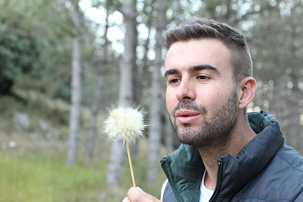 istock Guy blowing on white dandelion in nature 595736764