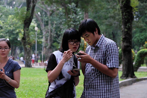 Ho Chi Minh City, Viet Nam - August 20, 2016: Young Asian couple play Pokemon go together on smart phone at Tao Dan park, hot virtual game for modern entertainment in technology life, danger for society