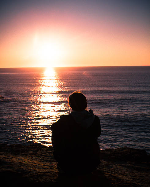 istock Young person sitting on a rocky cliff watching the sunset 595741670