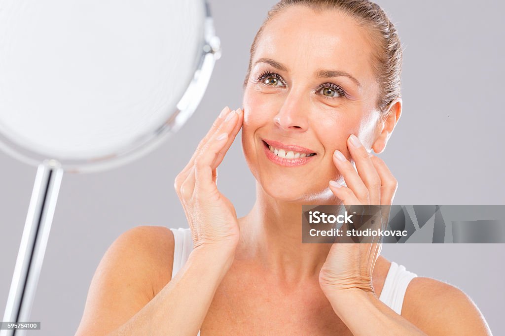 Mature woman, wrinkles and beauty. Mature woman with tenderness skin looking to the mirror.  Mature Women Stock Photo