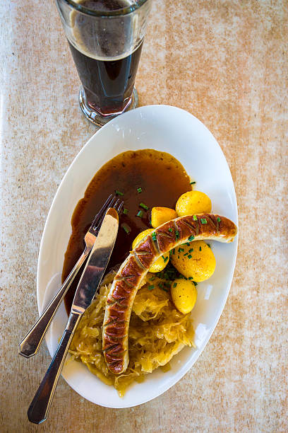 Sausage, stuffed sauerkraut, boiled potato and dark beer glass on table from directly above. German cuisine.