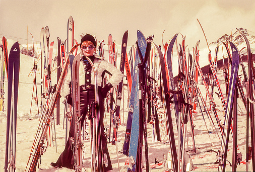 Vintage photo featuring a woman standing surrounded by skis on the snow.