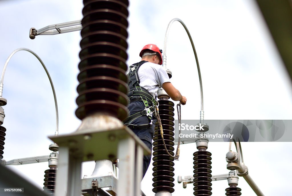 Electrician with Protective Workwear, Hardhat and Safety Harness Working Construction worker working in hight with protective equipment. Power Line Stock Photo