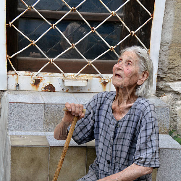 Varna, Bulgaria - August 8, 2016: Poor old woman in worn out, shabby dress sitting on stairs on the street