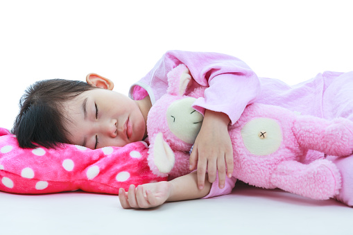 Healthy children concept. Closeup of asian child sleeping peacefully. Adorable girl in pink pajamas sleep tight on floor, on white background.