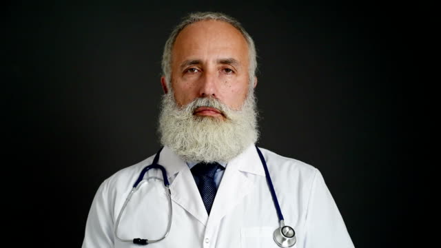 adult senior doctor  looking at the camera on a dark background