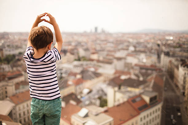 Photo of a little boy looking down on the city of Vienna from a window