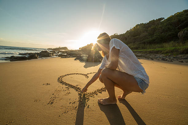 istock Female drawing heart shape on beach at sunrise 596044506