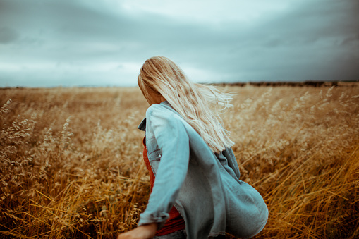 Photo of a young woman standing in the middle of a wheat field, walking away from her 