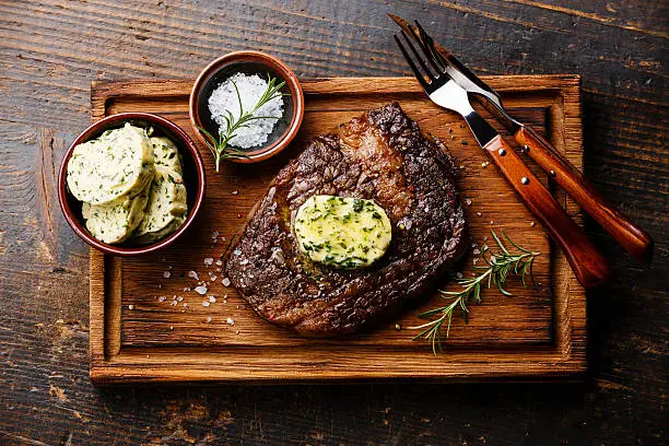 Sliced grilled steak Ribeye with herb butter on cutting board on wooden background