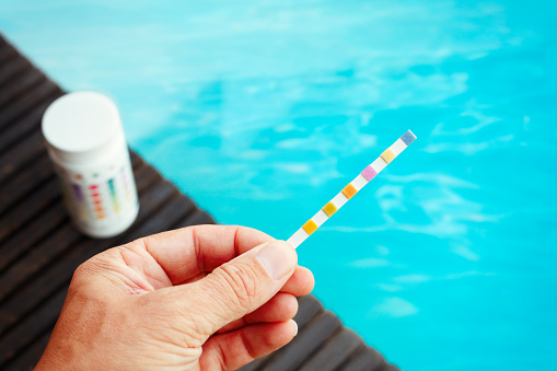 Person checking water quality with test strip in the swimming pool (chlorine, ph, hardness, alkalinity)