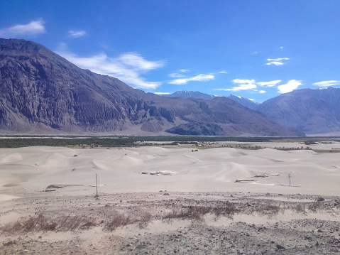 Beautiful scenic view of Nubra (Flower) valley desert - sand dunes against the background of distant colorful mountain range and cloudy blue sky, Ladakh, Himalaya, Jammu & Kashmir, Northern India