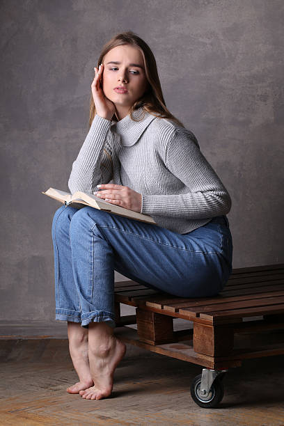 istock Girl in sweater holding book and sitting on a deck 596060346