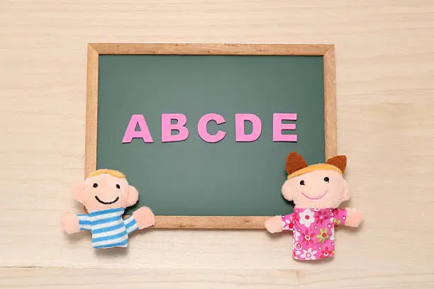 Photo of Alphabet letters ABCDE and children dolls on blackboard.