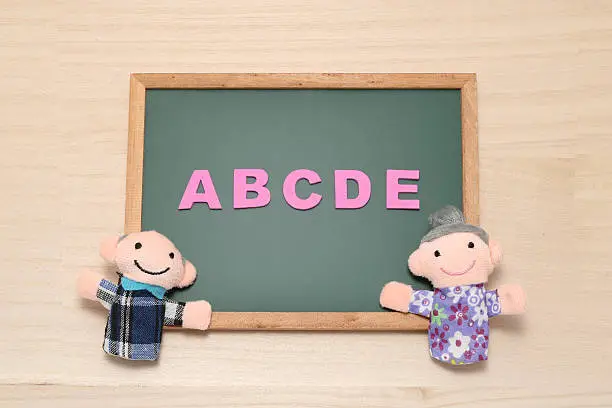 Photo of Alphabet letters ABCDE and elderly dolls on blackboard.