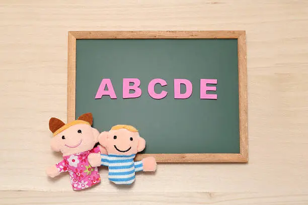 Photo of Alphabet letters ABCDE and children dolls on blackboard.