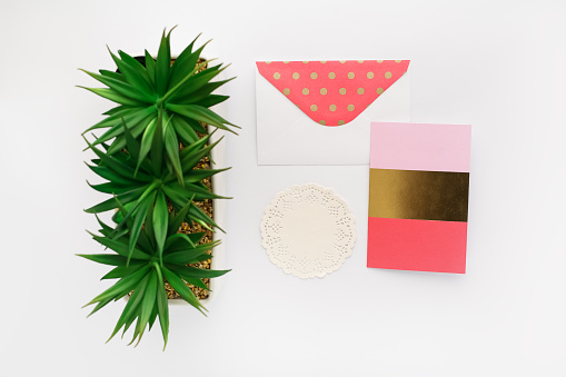 Gold and coral polka dot envelope with matching greeting card beside a plant and cream textured doily.