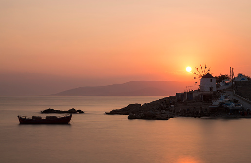 Magnificent red sunset over a fishing village in Kofounisa island, with the Greek traditional windmill, the small chapel and fishing boat as the main features.