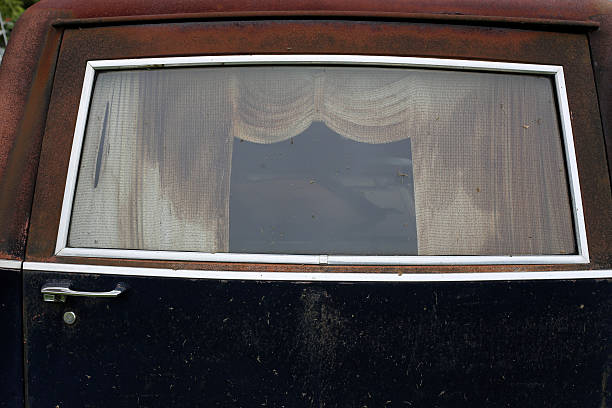 Creep old window frame on the back of a hearse. Shows rotting and faded curtains.