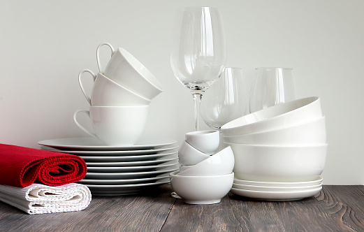 White dishware stacked on a wooden table against black background with transparent wineglasses