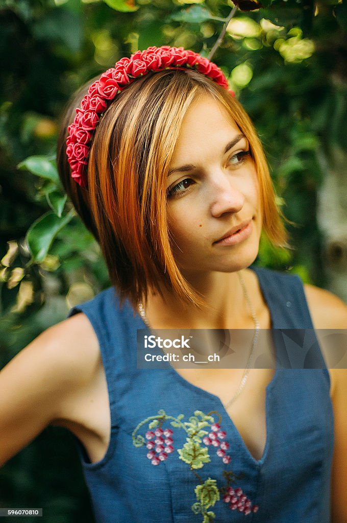 Portrait of a beautiful young woman wearing Portrait of a beautiful young woman wearing wreath. Young beautiful woman posing with flowers bouquet on her head. Girl posing in a decorative wreath of artificial flowers on outdoor in the summer Adult Stock Photo