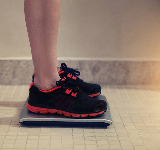 istock Female bare feet with weight scale 596075378