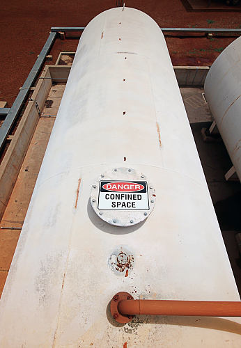 A sign warns of the dangers of a confined space within a large industrial tank.