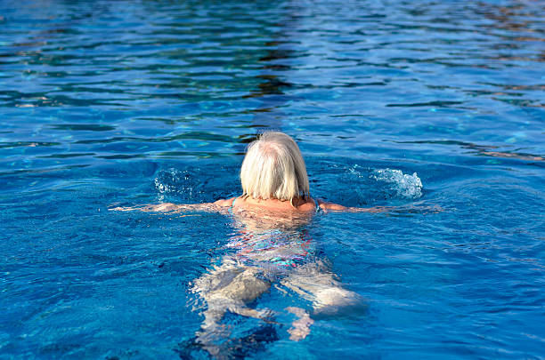 mujer mayor activa nadando en una piscina - braza fotografías e imágenes de stock