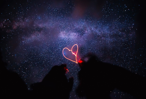 Two silhouettes under the milky way. Heart painted with light.