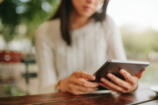 Shot of young female sitting at cafe table. Woman using tablet at coffee shop. Focus on digital tablet.