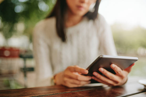 Young female sitting at cafe table with digital tablet Shot of young female sitting at cafe table. Woman using tablet at coffee shop. Focus on digital tablet. jacob ammentorp lund stock pictures, royalty-free photos & images