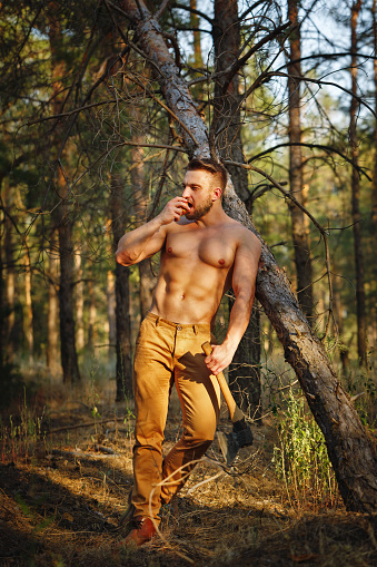 Lumberjack eating an apple. Woodcutter with a naked torso and ax in his hands. Felling trees. Logging. Manual labor.