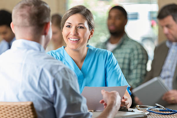 Manager at hospital  interviewing potential nursing staff healthcare worker Mid adult woman is manager of at hospital. She is reading a resume and interviewing a potential nursing staff employee. Other candidates are waiting to be interviewed during hospital's staff recruitment event. interview event stock pictures, royalty-free photos & images