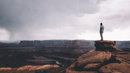 Man standing on the top of the rock overlooking Canyonlands enjoying the vast landscape view.