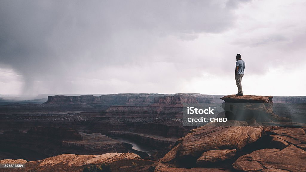 On the edge of Canyonlands Man standing on the top of the rock overlooking Canyonlands enjoying the vast landscape view. Cliff Stock Photo