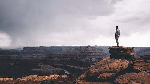 On the edge of Canyonlands Man standing on the top of the rock overlooking Canyonlands enjoying the vast landscape view. canyon stock pictures, royalty-free photos & images