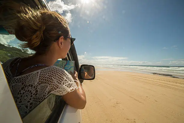 Young woman in a car reads a road map, Fraser Island.