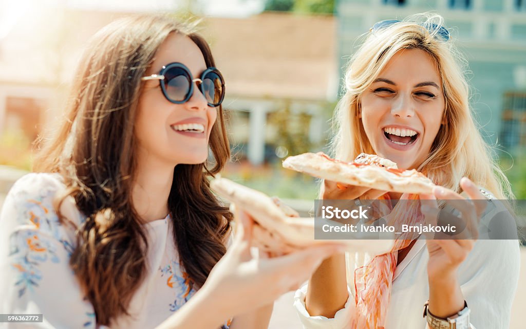 Friends eating pizza Portrait of two young women eating pizza outdoors Pizza Stock Photo