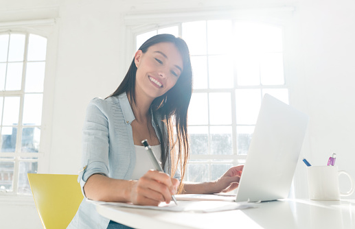 Happy Latin American woman paying bills online at home using a laptop computer