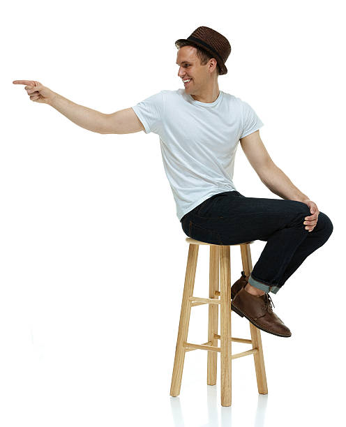 istock Smiling hipster on stool and pointing away 596374284