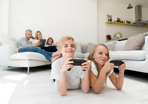 Happy kids having fun playing video games at home with their family at the background