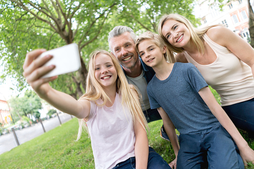 Happy Caucasian family taking a selfie at the park with a mobile phone